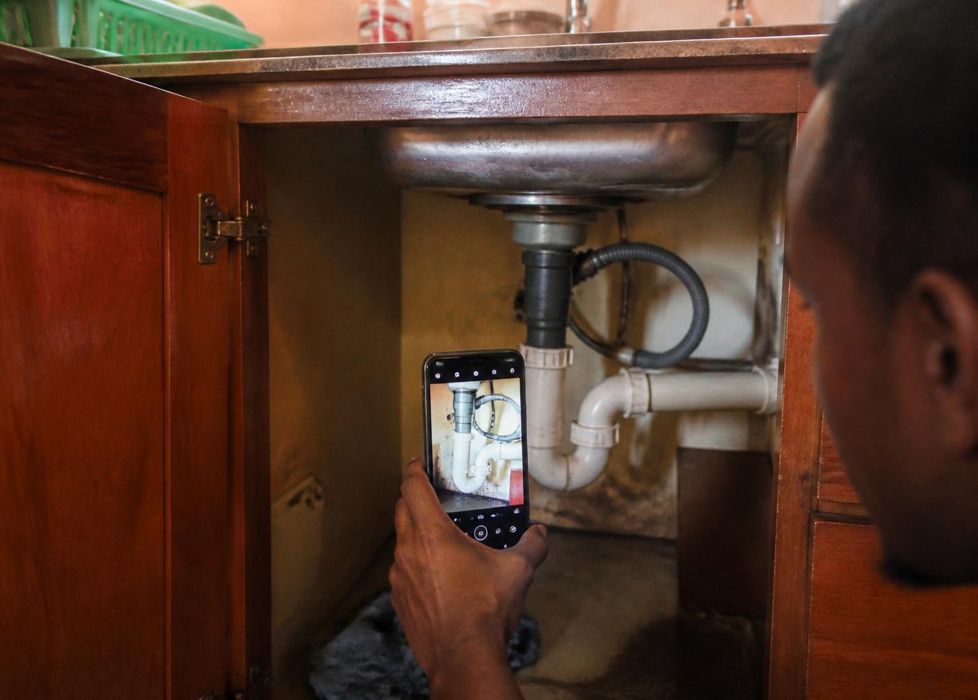 A technician photographing a repaired pipe under a kitchen sink